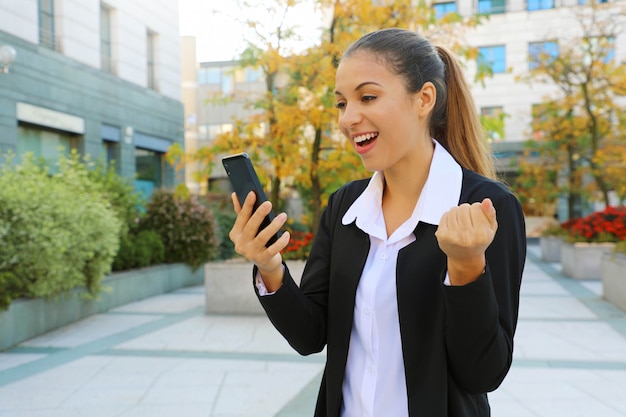 Молодая успешная бизнес-леди, держащая умный телефон на открытом воздухе.