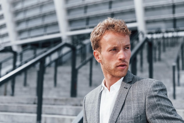 Young successful businessman in grey formal wear is outdoors in the city