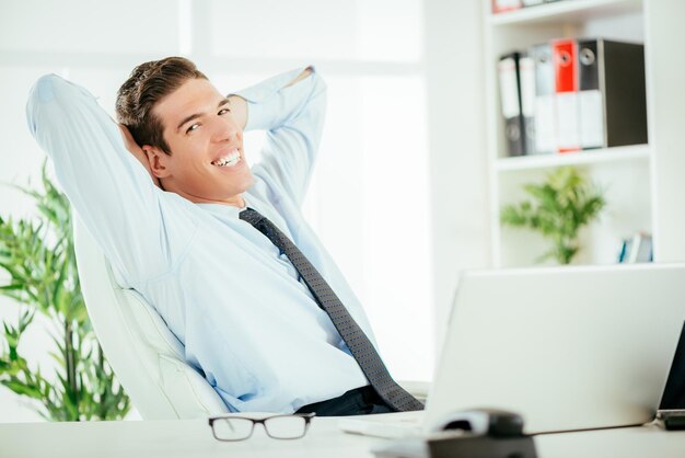 Young successful businessman relaxing in the office with hands behind  head and looking at camera.