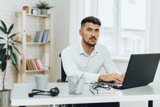 Young successful businessman using laptop at his office desk close up