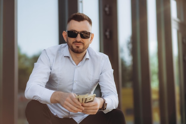 Photo young successful businessman working on laptop bearded man in business suit looking at camera and smiling talking on the phone near a modern office center outside