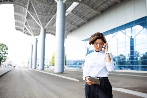 Young successful businesswoman speaking on phone standing near business centre