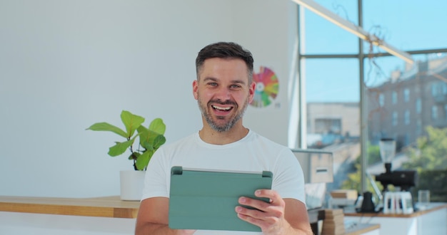 Young successful cafe owner standing in cafe using digital tablet while accepting online order Coffee shop concept