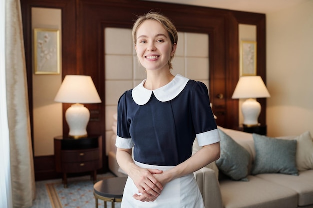 Young successful chambermaid in uniform standing in front of camera