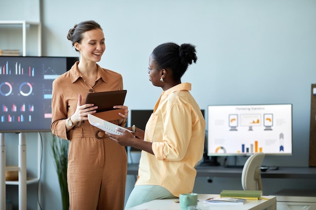 Young successful coach with tablet looking at african american
female employee while consulting her