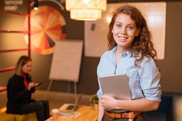 Young successful female employee with touchpad standing in office