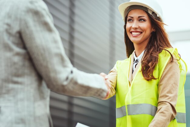 Young successful female engineer with white helmet shaking hands with manager and celebrating its success.