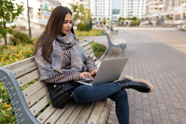 Giovane libero professionista femminile di successo che lavora su un computer portatile sullo sfondo di un parco cittadino seduto