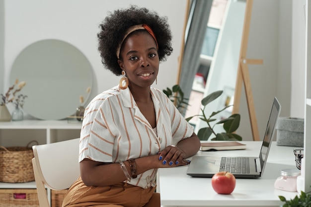 Young successful female sitting by desk in front of laptop