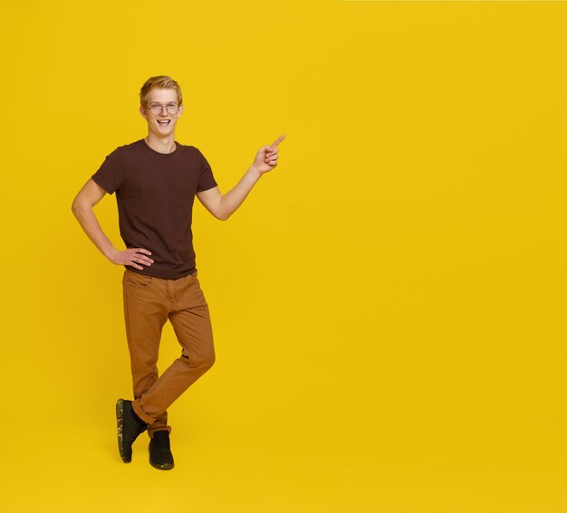 Young successful guy appoints to empty place for copy space man smiling isolated on yellow