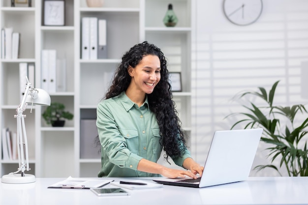 Young successful hispanic businesswoman working in bright home office indoors sitting at table with