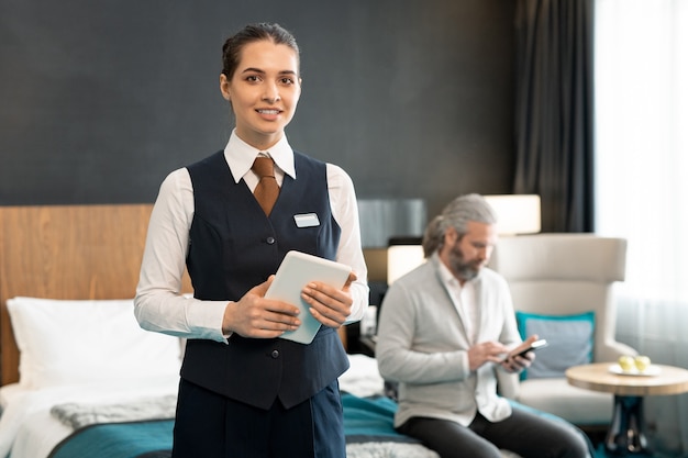 Photo young successful hotel manager with touchpad standing against mature male client