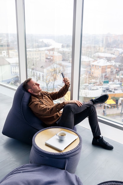 Young successful male businessman is sitting near a large window in the office and relaxing. Rest after a working day