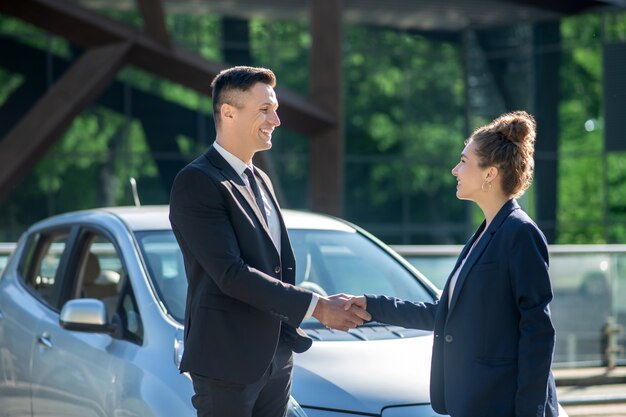 Young successful man and woman hand in hand near car