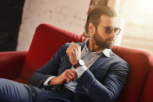 Photo young and successfulbusinessman is sitting on sofa in modern office and looking away through