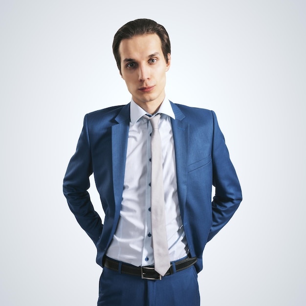 Young successfull businessman in blue suit and grey tie on light background close up