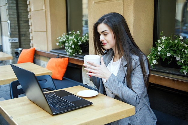 Young sucsessful business woman drinking coffee during work at the street cafeteria