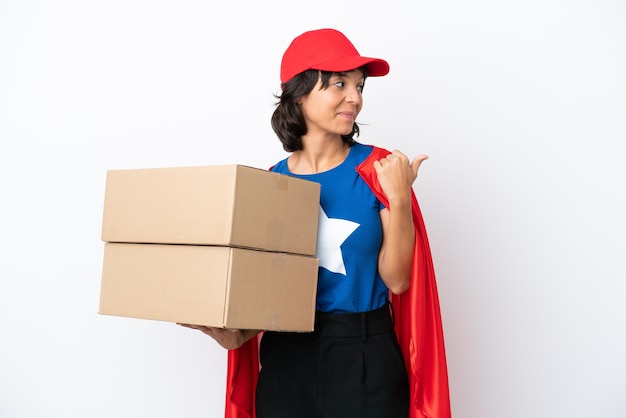 Young superhero delivery girl isolated on pink background pointing to the side to present a product