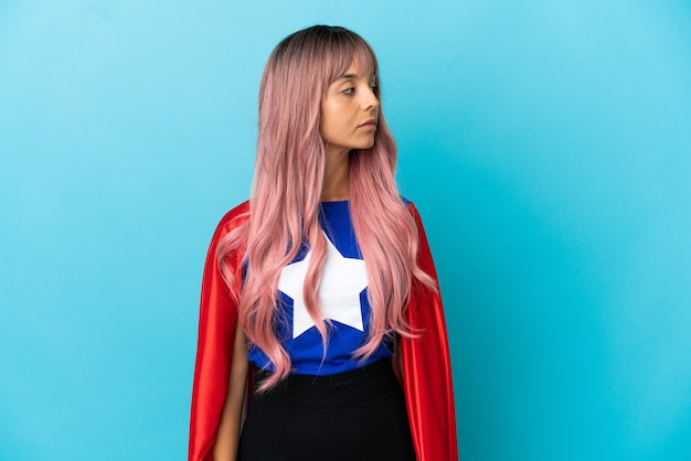 Young superhero woman with pink hair isolated on blue background looking to the side