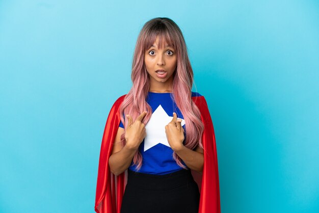 Young superhero woman with pink hair isolated on blue background with surprise facial expression