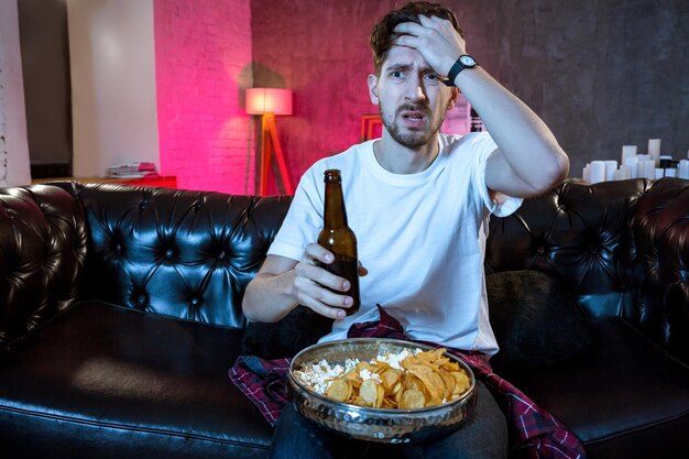 Young supporter man watching football game on television sitting