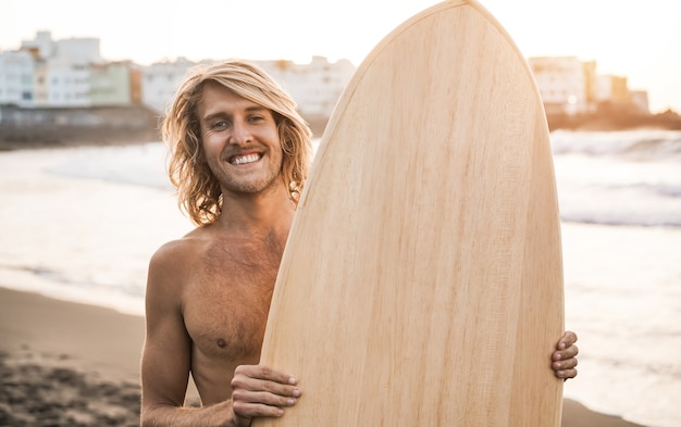 Young surfer man holding surf board on the beach at summer sunset 