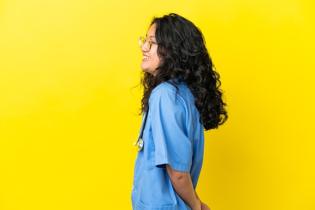 Young surgeon doctor asian woman isolated on yellow background laughing in lateral position