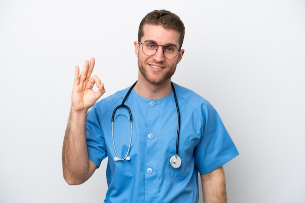 Молодой врач-хирург, кавказец, изолированный на белом фоне, показывает пальцами знак "ок"