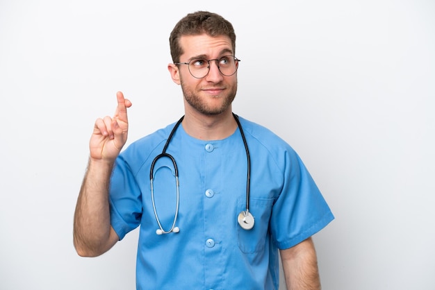 Young surgeon doctor caucasian man isolated on white background with fingers crossing and wishing the best