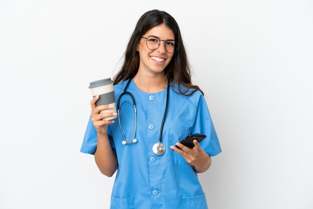 Young surgeon doctor caucasian woman isolated on white background holding coffee to take away and a mobile