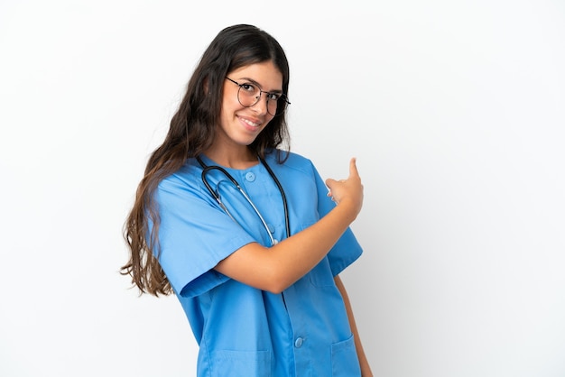 Young surgeon doctor caucasian woman isolated on white background pointing back