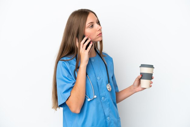 Young surgeon doctor Lithuanian woman isolated on white background holding coffee to take away and a mobile