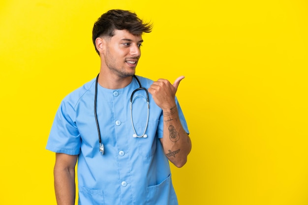 Young surgeon doctor man isolated on yellow background pointing to the side to present a product