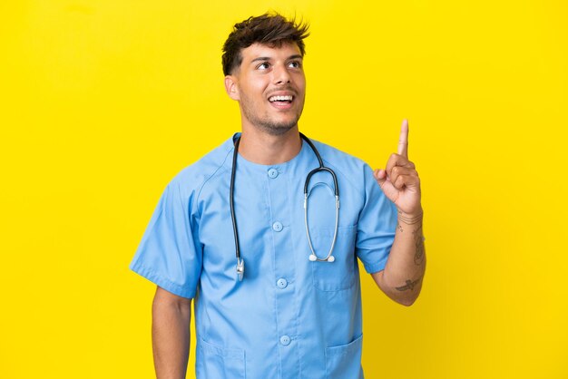 Young surgeon doctor man isolated on yellow background pointing up and surprised