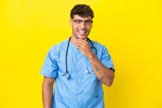 Young surgeon doctor man isolated on yellow background with glasses and smiling