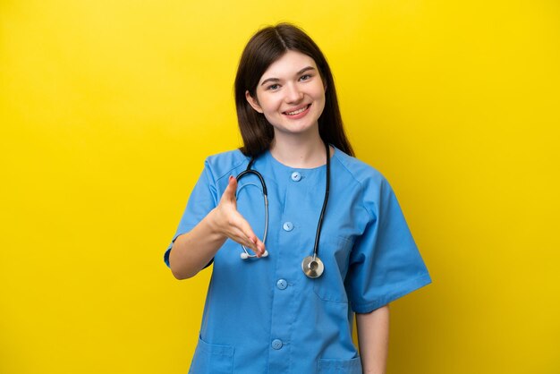 Giovane medico chirurgo donna russa isolata su sfondo giallo che stringe la mano per chiudere un buon affare