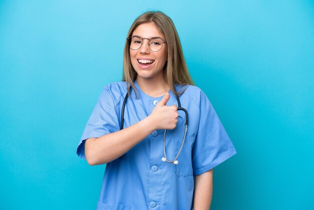 Young surgeon doctor woman isolated on blue background giving a thumbs up gesture