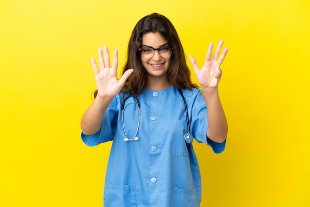 Giovane donna medico chirurgo isolata su sfondo giallo contando nove con le dita