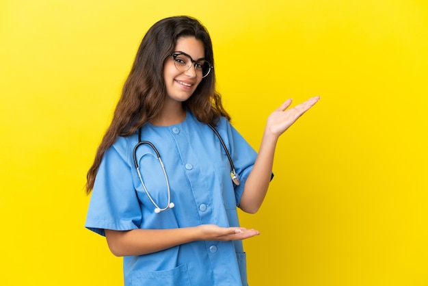 Young surgeon doctor woman isolated on yellow background extending hands to the side for inviting to come