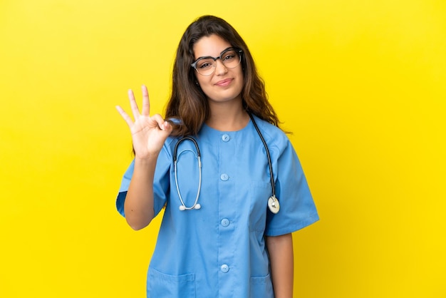 Young surgeon doctor woman isolated on yellow background happy and counting three with fingers