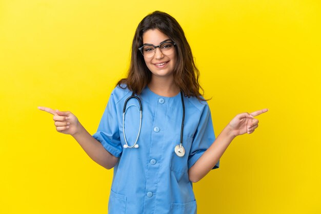 Young surgeon doctor woman isolated on yellow background pointing finger to the laterals and happy