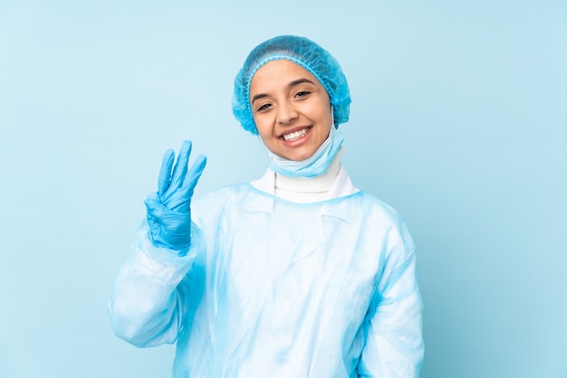 青い制服を着た幸せと指で3つを数える若い外科医インドの女性