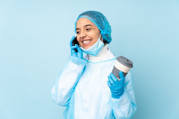 Young surgeon Indian woman in blue uniform holding coffee to take away and a mobile