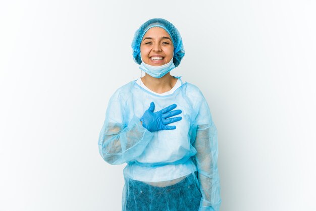 Young surgeon latin woman isolated on white laughs out loudly keeping hand on chest.