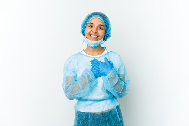 Young surgeon latin woman isolated on white wall has friendly expression, pressing palm to chest. Love concept.