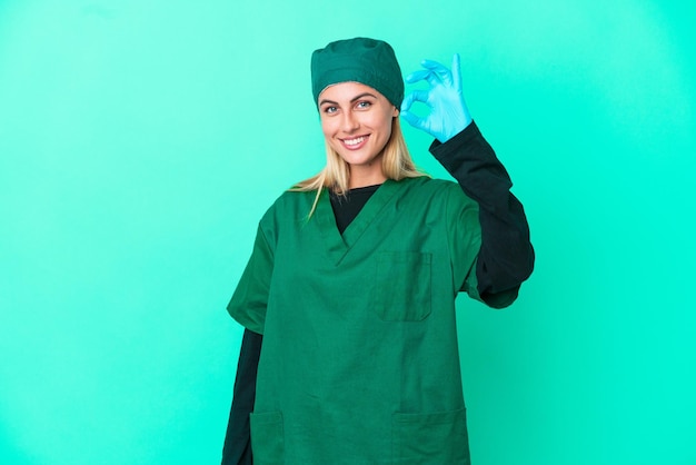 Young surgeon Uruguayan woman in green uniform isolated on blue background showing ok sign with fingers