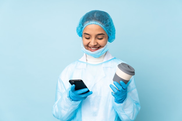 Young surgeon woman in blue uniform holding coffee to take away and a mobile