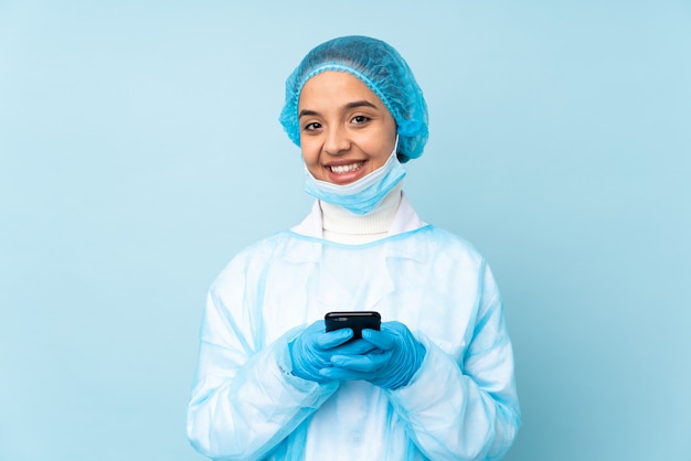 모바일과 메시지를 보내는 파란색 유니폼을 입고 젊은 외과 의사 여자