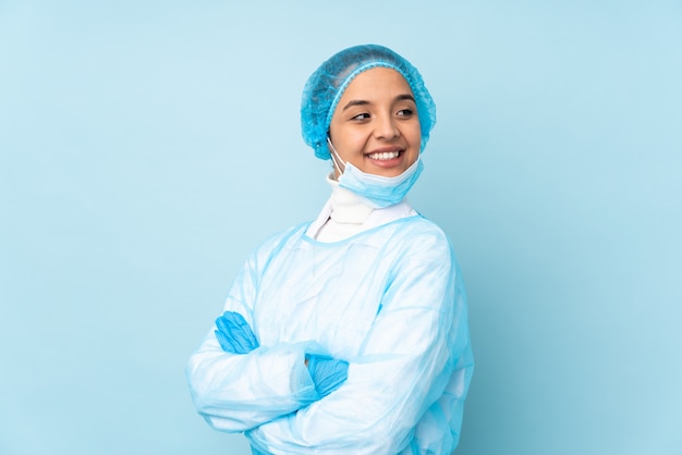 Young surgeon woman in blue uniform with arms crossed and happy