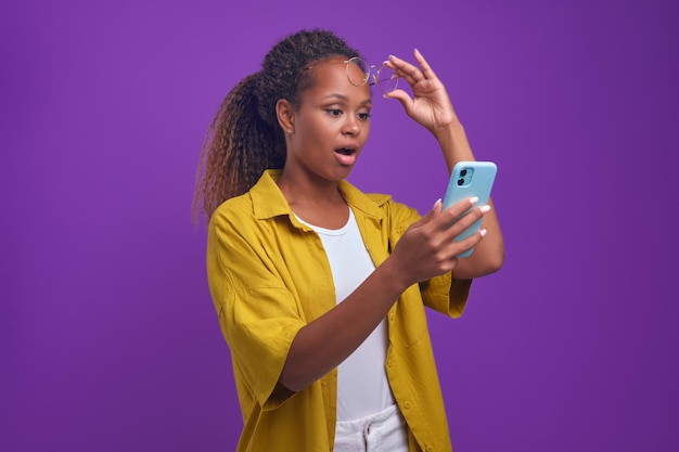 Young surprised african american woman holding mobile phone with opens mouth